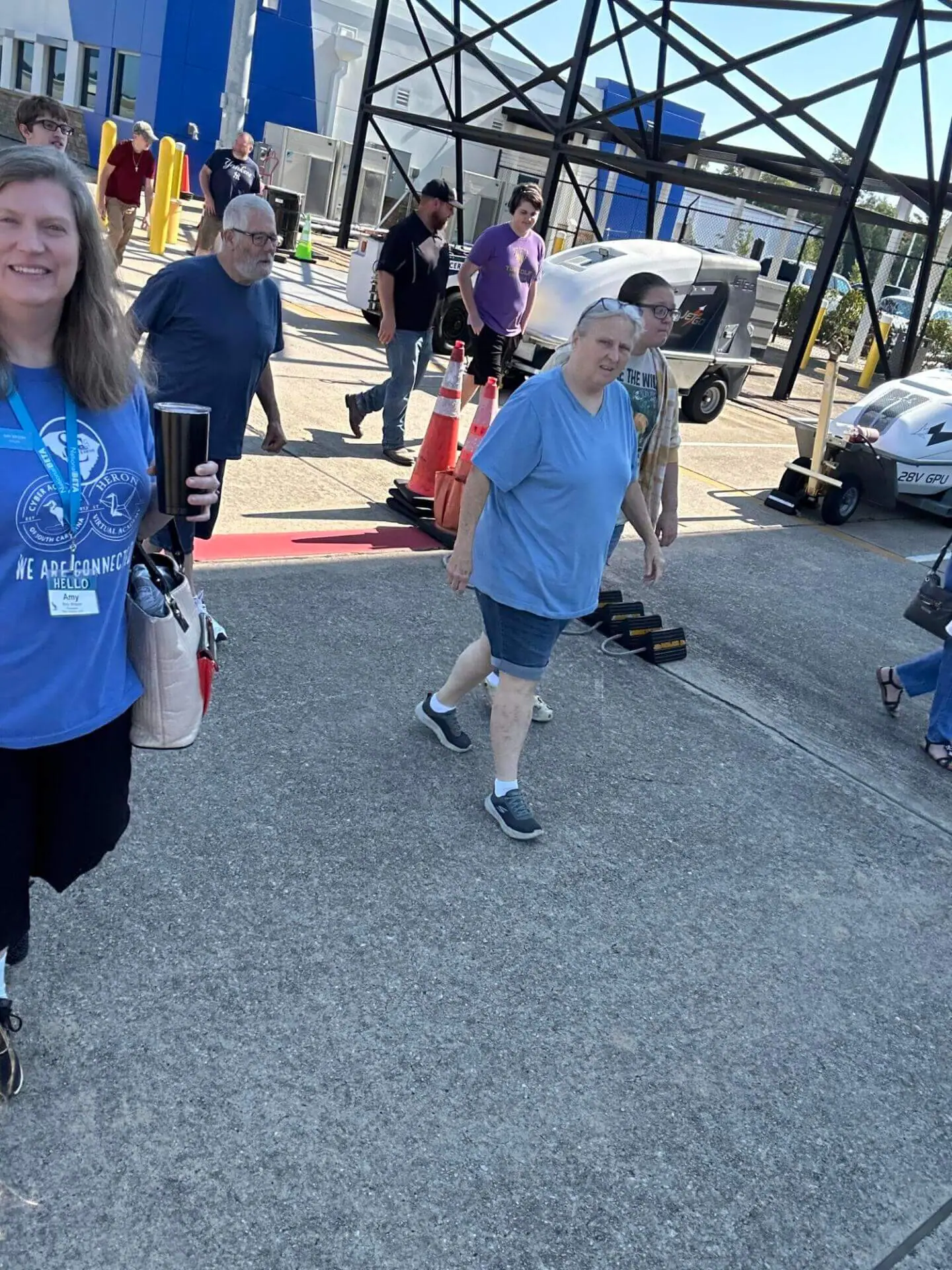A group of people walks outdoors on a sunny day, surrounded by industrial structures.