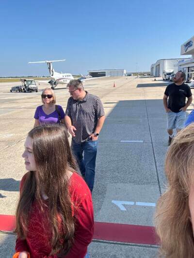 People standing on an airport tarmac, a small plane in the background.