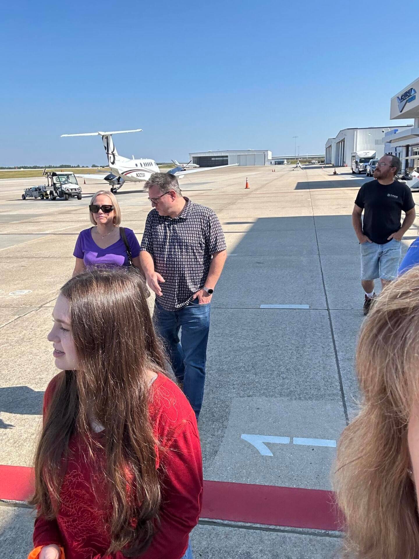 People standing on an airport tarmac, a small plane in the background.