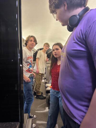 Four young people stand inside an aircraft aisle.