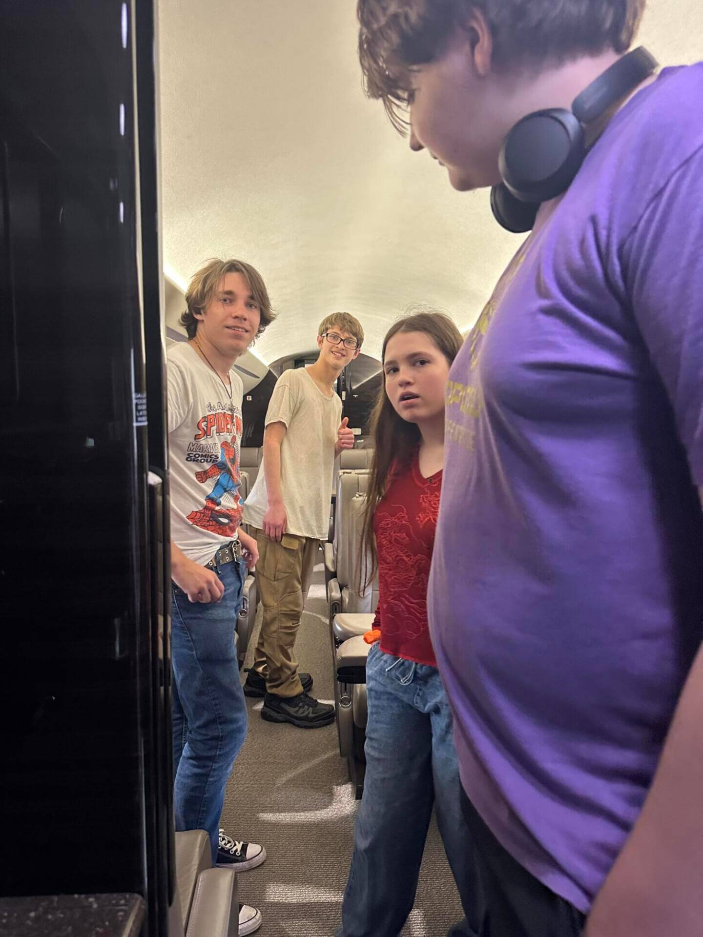 Four young people stand inside an aircraft aisle.
