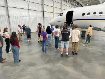 A group of people stands attentively near a small jet in a spacious hangar.