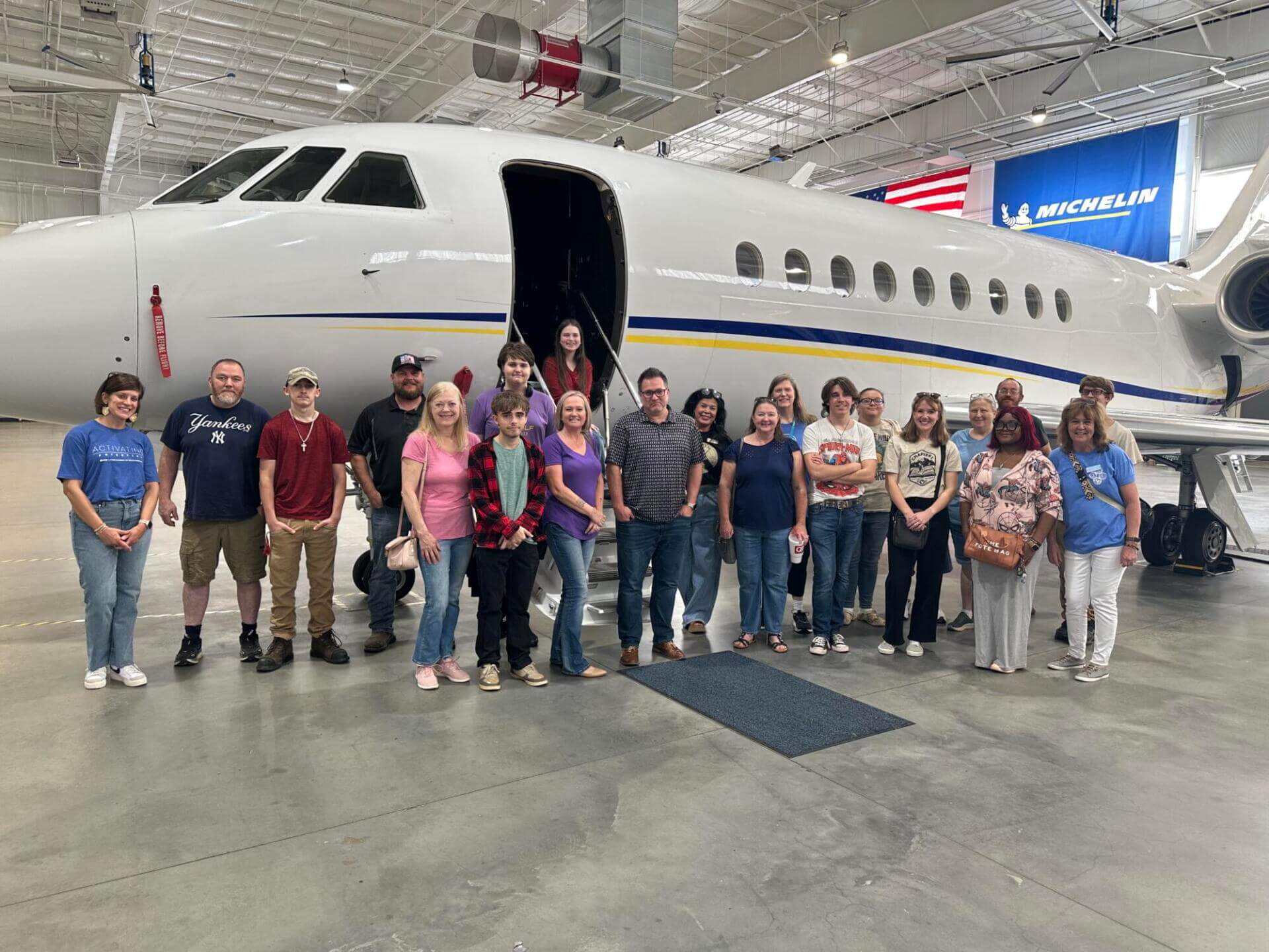 A group of people stands smiling in front of a sleek private jet inside an aircraft hangar.