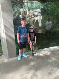 Two smiling boys stand in front of a zoo enclosure.