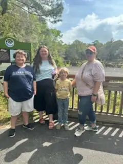 A group of four people, including a child, stand on a sunny boardwalk in a park.