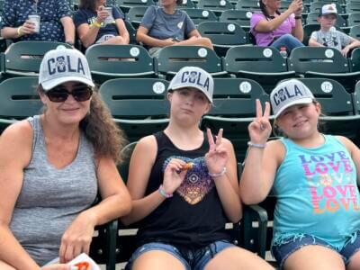 Three people wearing "COLA" caps sit in a stadium.