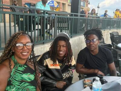 A woman and two young men smile at an outdoor event.
