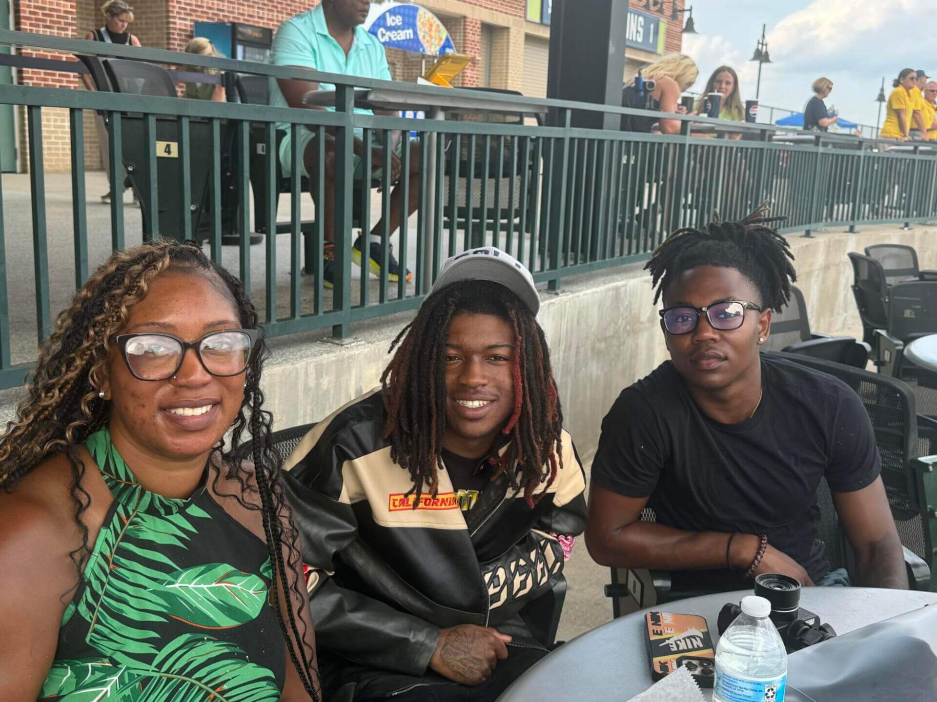 A woman and two young men smile at an outdoor event.