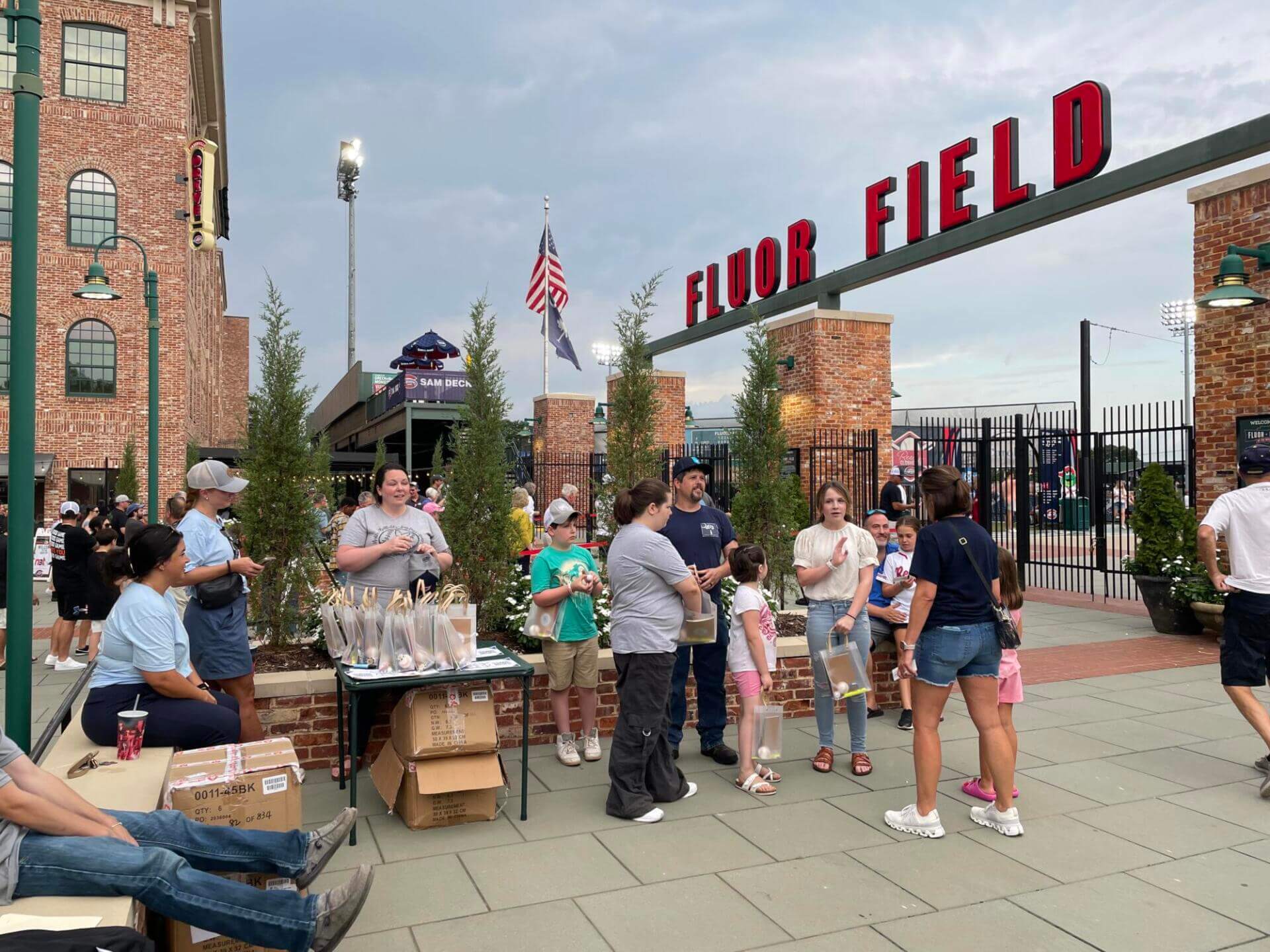 A diverse group of people gathers near the entrance of Fluor Field, enjoying a casual outdoor event.