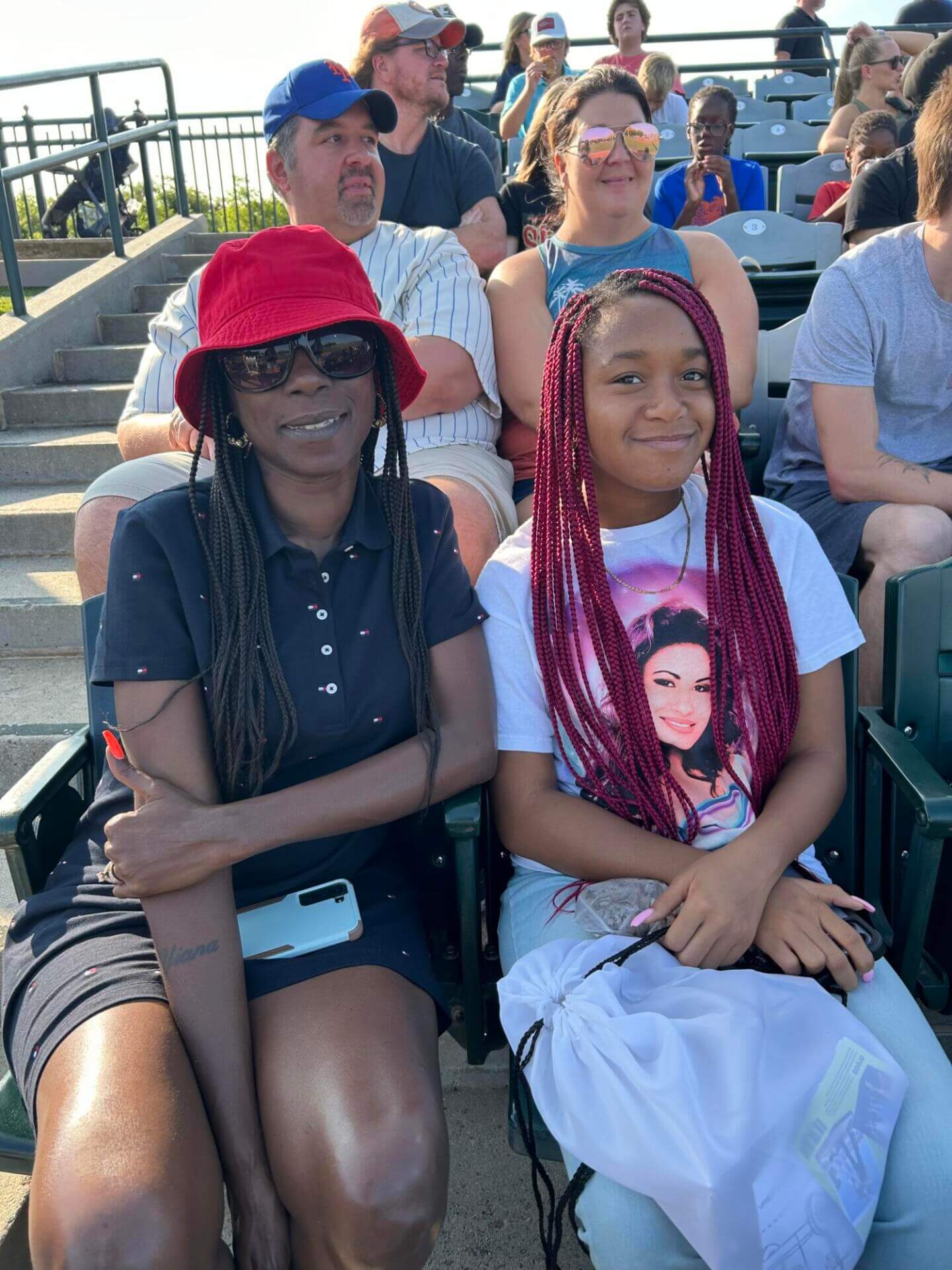 Two people sit closely together in a sunny outdoor setting, smiling.