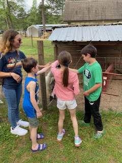 Four children and an adult pet a goat outside a barn.