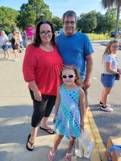 A smiling family stands outdoors.