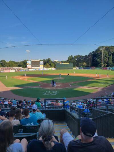 Baseball game in progress on a sunny day. Fans seated in a stadium watch players on the field.
