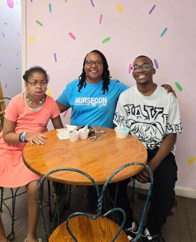 A smiling group of three people sits at a round wooden table with ice cream cups.