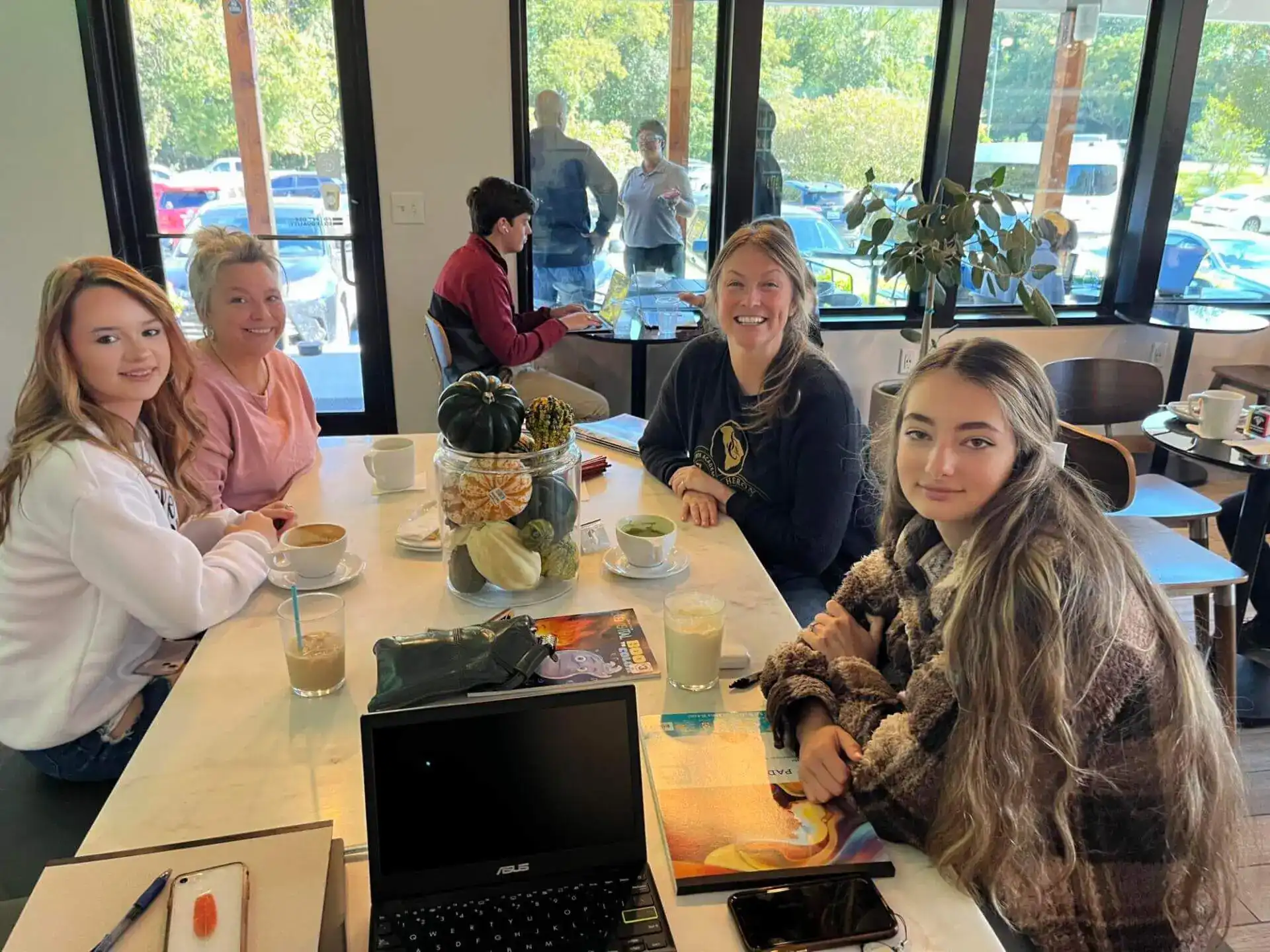 Four people smile around a café table with coffee and a laptop open