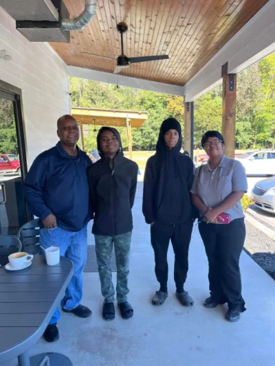 A family of four stands on a porch under a wooden ceiling.
