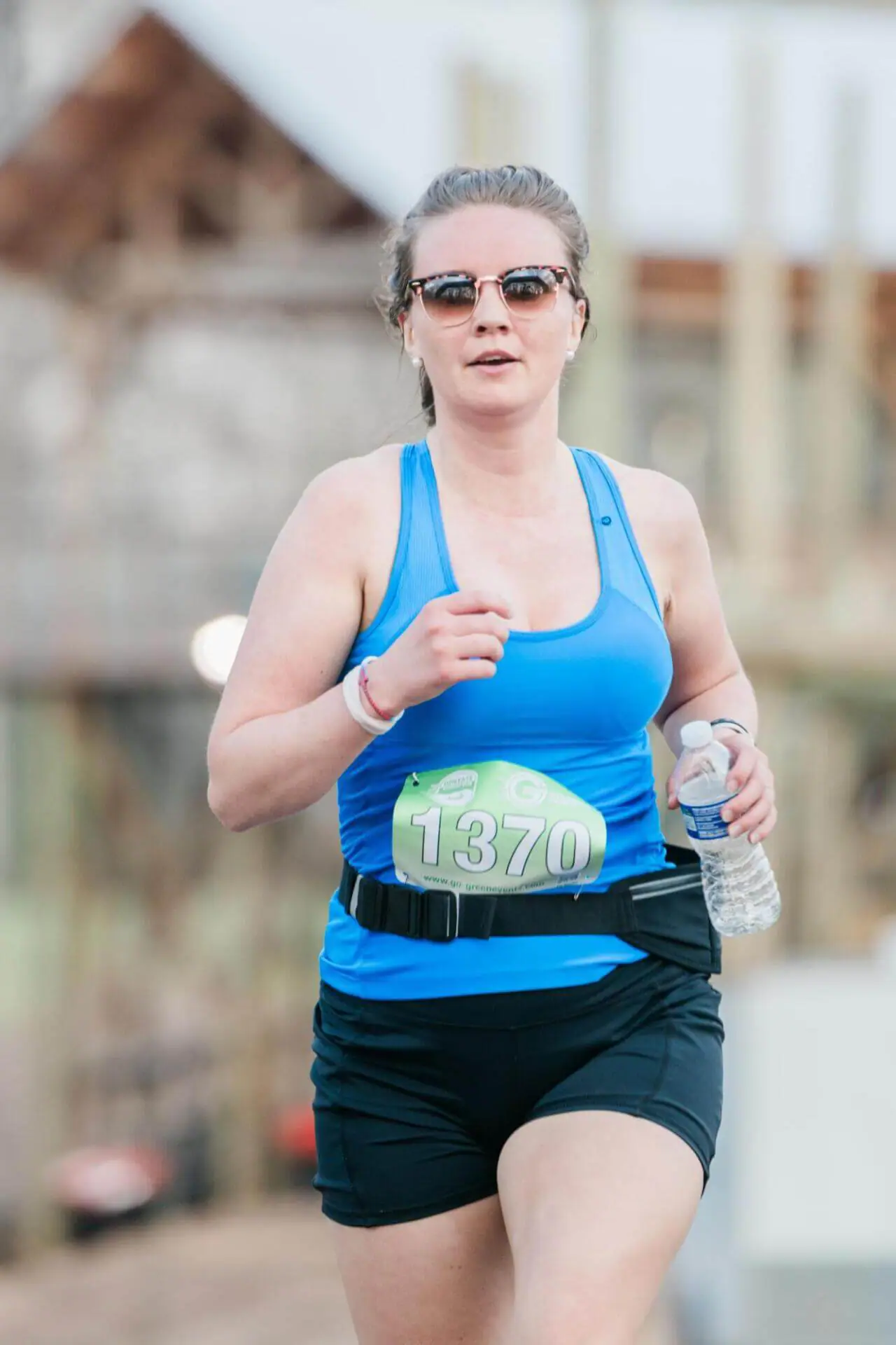 Woman wearing glasses running with a bottle of water on her hand