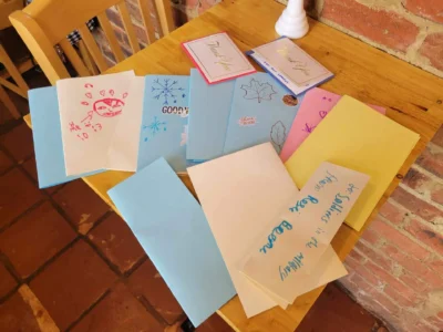 A variety of handmade cards with colorful drawings and messages are spread across a wooden table.