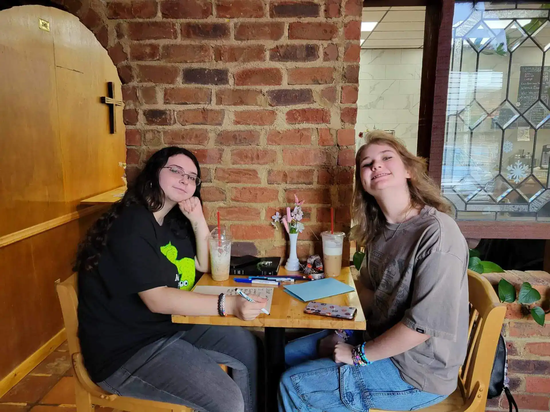 Two people sit at a wooden table in a cozy café with exposed brick walls.