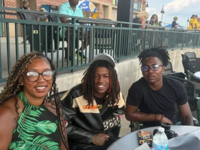 A woman and two young men smile at an outdoor event.